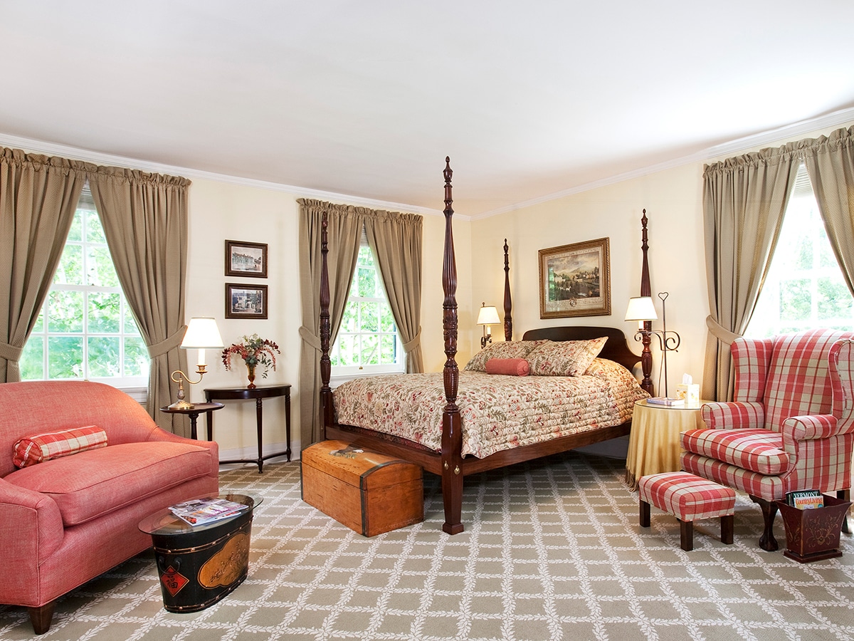carved four poster maple bed with a red and white plaid armchair and stool, a domed top chest is at the foot of the bed